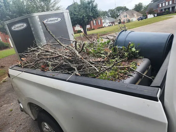 White truck bed filled with branches and a blue barrel. Trailer is visible.
