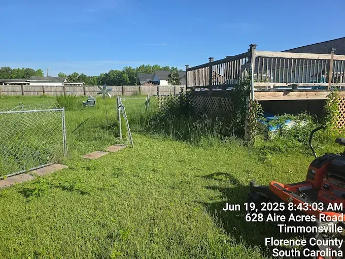 Backyard with tall grass, wooden deck, chain-link fence, and a lawnmower in Timmonsville, SC.