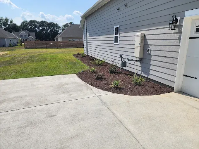 Concrete driveway and side of a gray house with a flowerbed.
