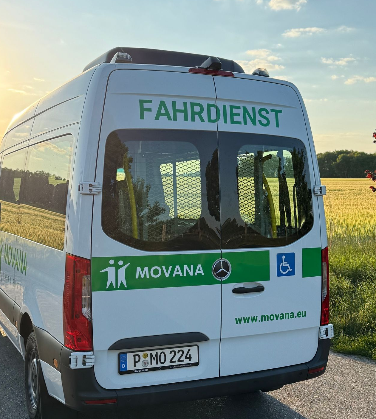 Rückseite eines weißen Movana Fahrdienst-Sprinters mit grünen Akzenten und Rollstuhlzugänglichkeitssymbol neben einem Feld.