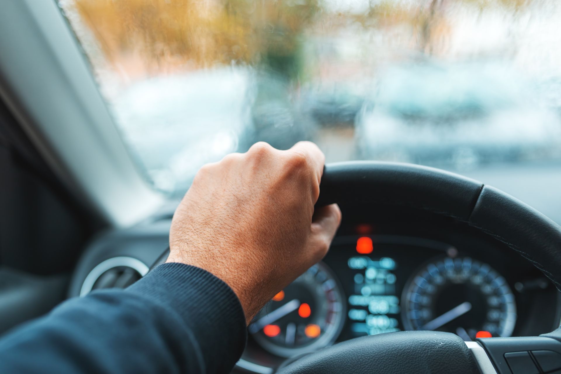 Eine Hand umklammert ein Lenkrad in einem Auto, das Armaturenbrett ist durch die Windschutzscheibe sichtbar.