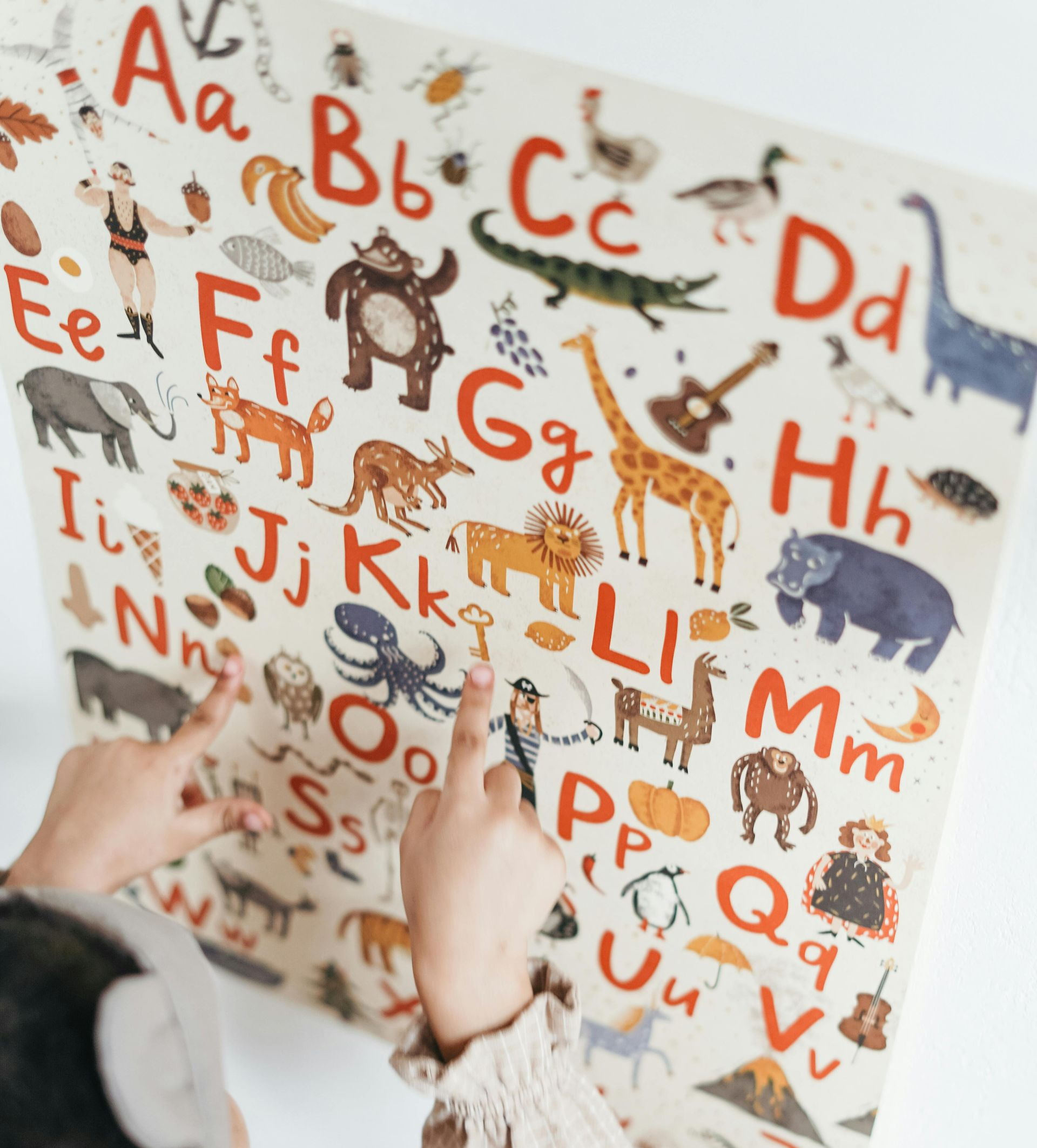 Kind zeigt auf eine Alphabettabelle mit Tierillustrationen; beiger Hintergrund, rote und braune Schrift.