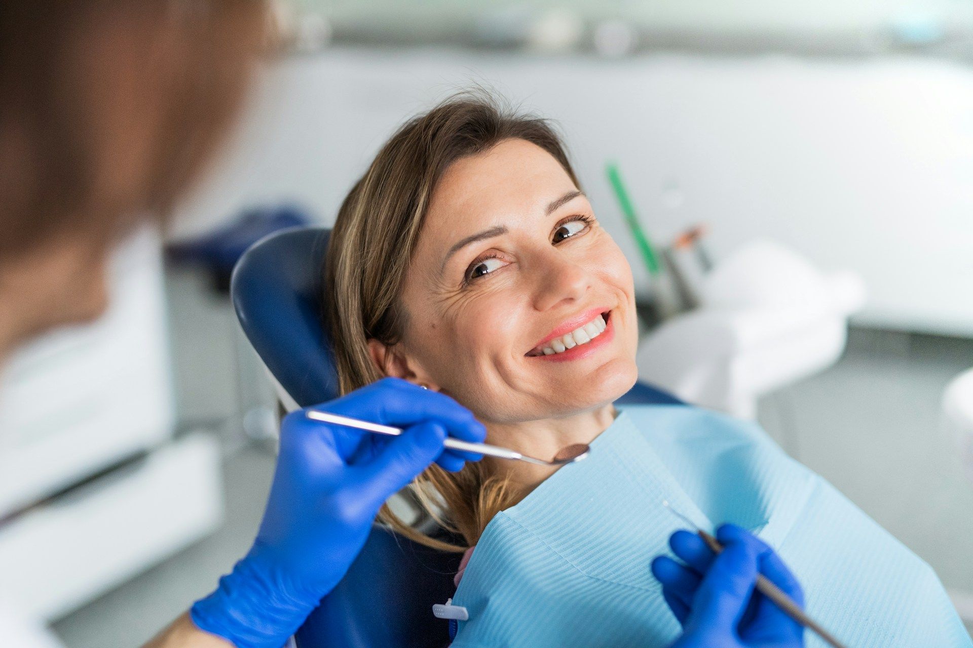 A woman is sitting in a dental chair while a dentist applies dental veneers.