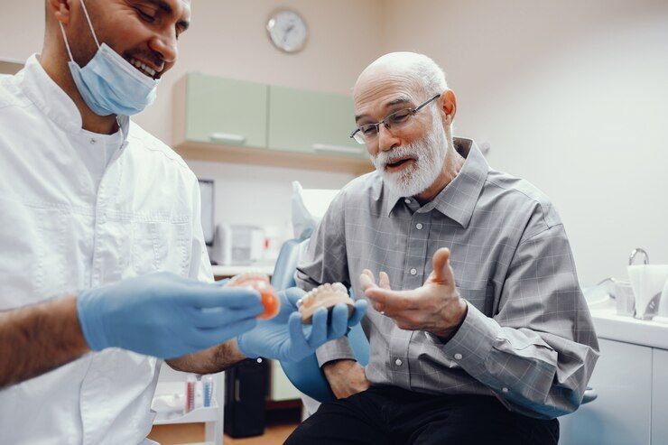 A dentist is showing an elderly man a dental implant model.