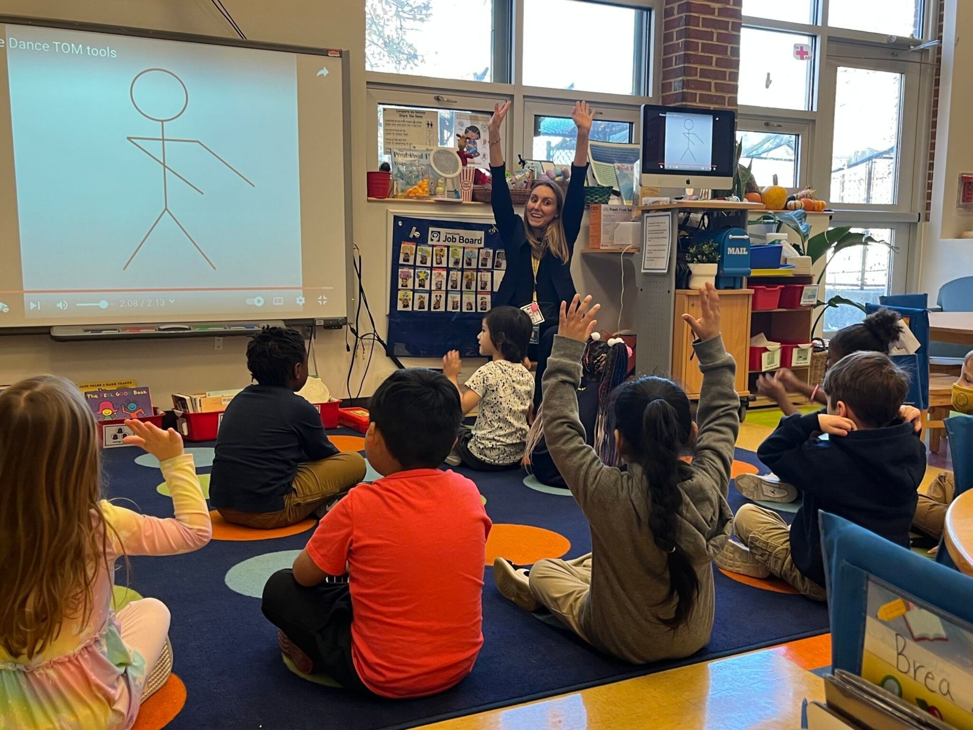 Kids and teacher in a classroom with hands raised