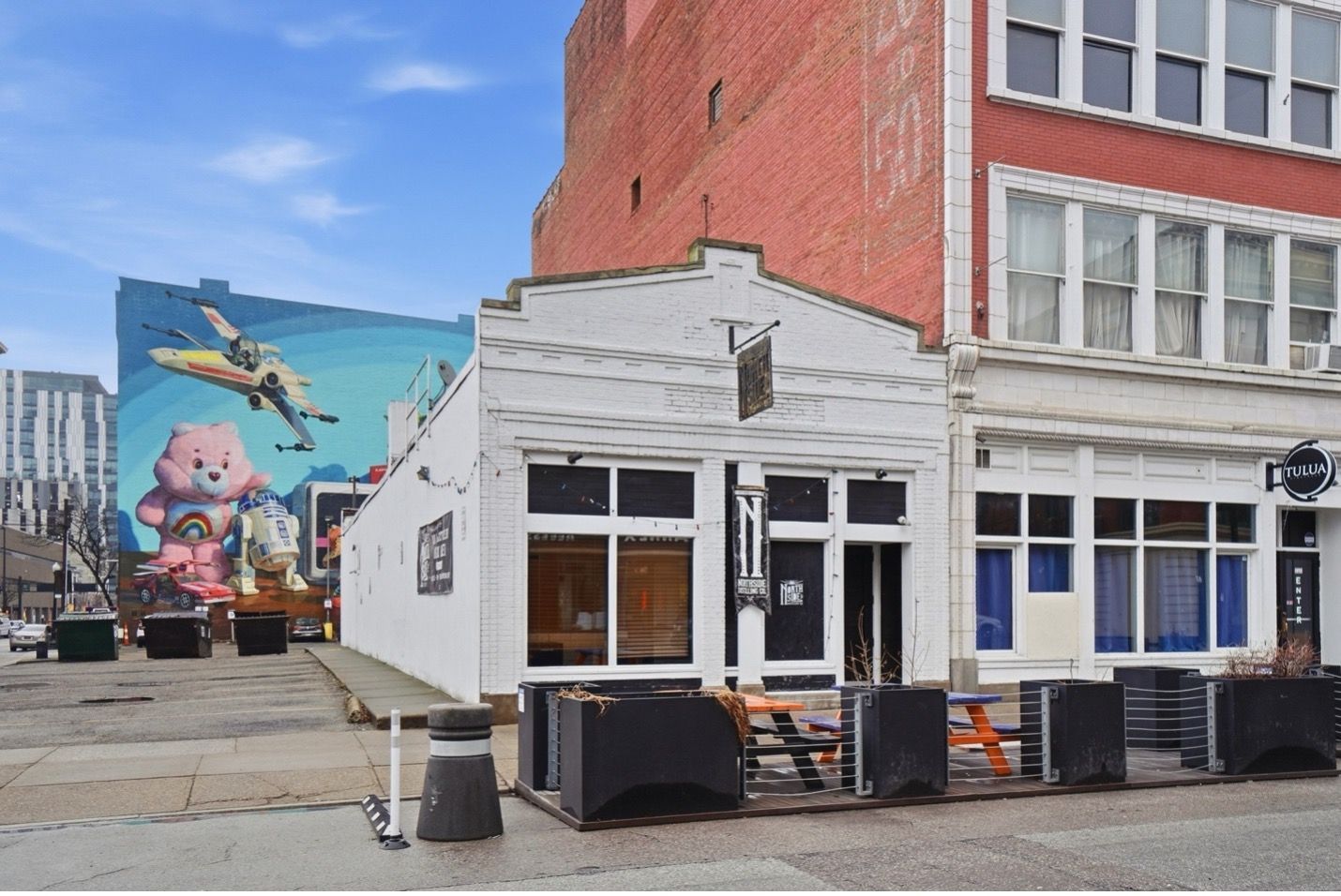 Red brick multi-story building with multiple rectangular windows against a blue cloudy sky.
