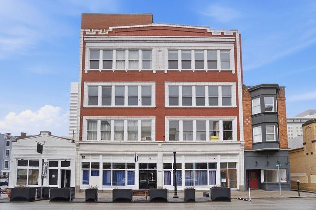 Red brick multi-story building with multiple rectangular windows against a blue cloudy sky.