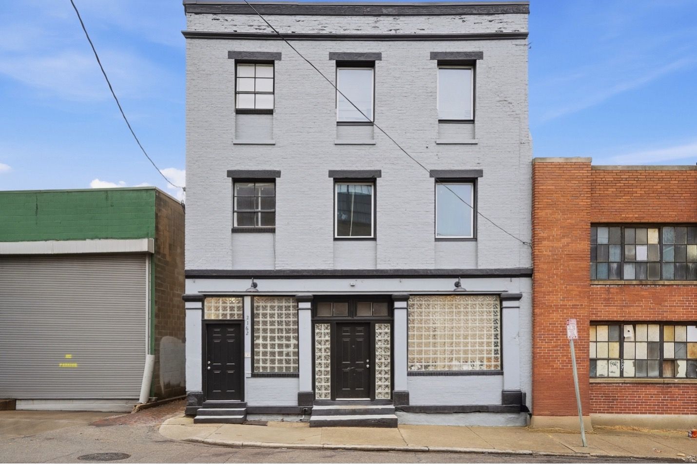 Modern apartment building with brown and white facade, balconies, and blue accents against a bright sky.
