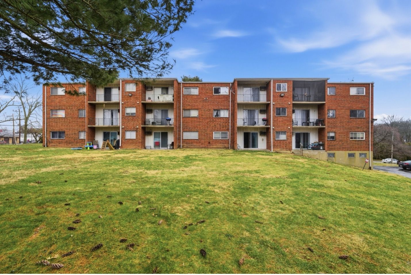 Modern apartment building with brown and white facade, balconies, and blue accents against a bright sky.