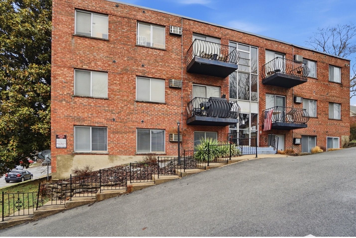 Red brick multi-story building with multiple rectangular windows against a blue cloudy sky.