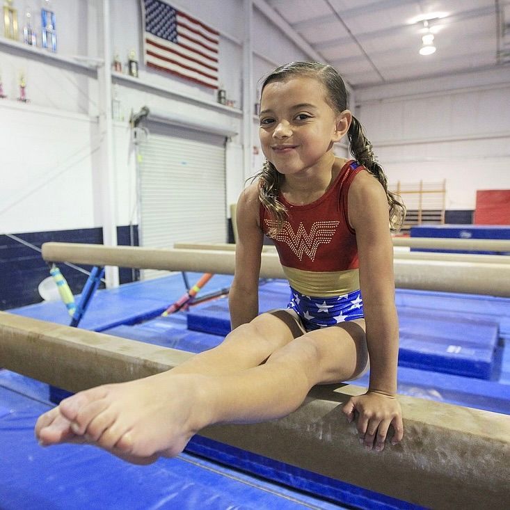 A young girl is sitting on a balance beam in a gym