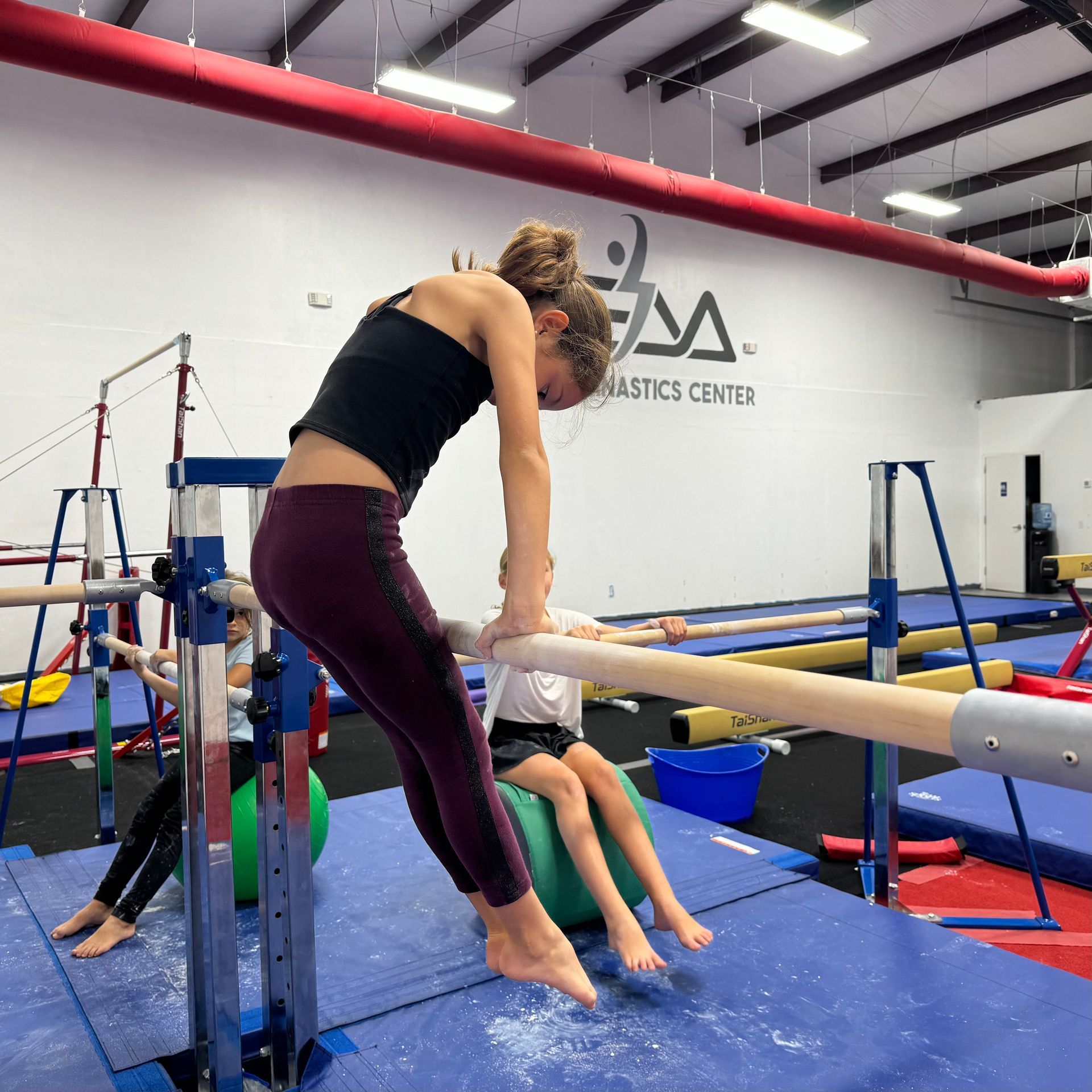 A woman is doing a handstand on a bar in a gymnastics center