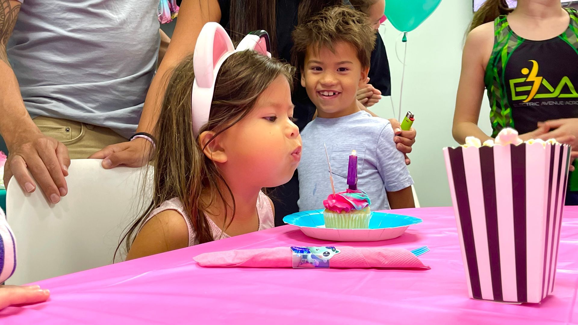 A little girl is blowing out a candle on a cupcake at a birthday party.