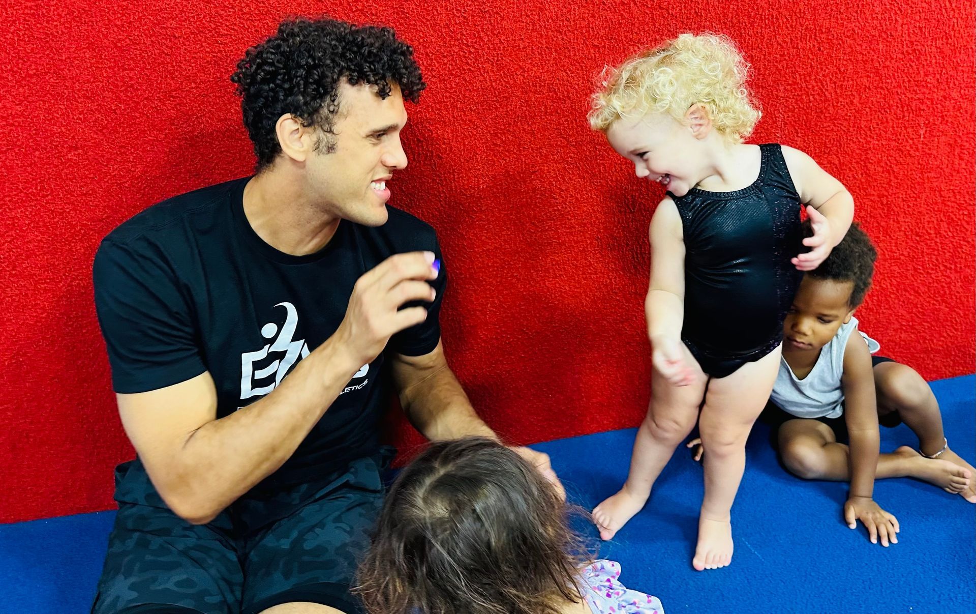 A man is sitting on the floor talking to two little girls.