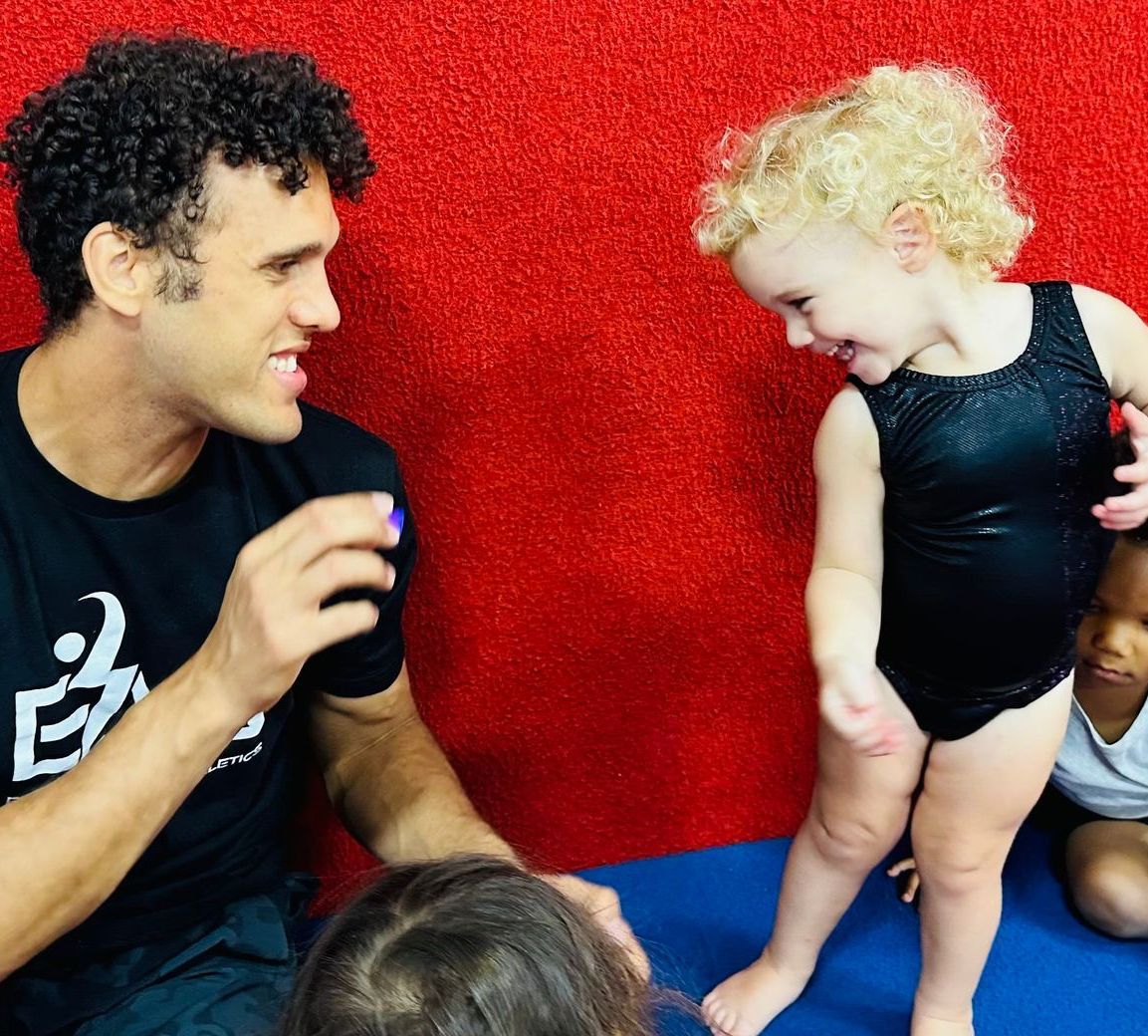 A man is talking to a little girl who is wearing a black leotard