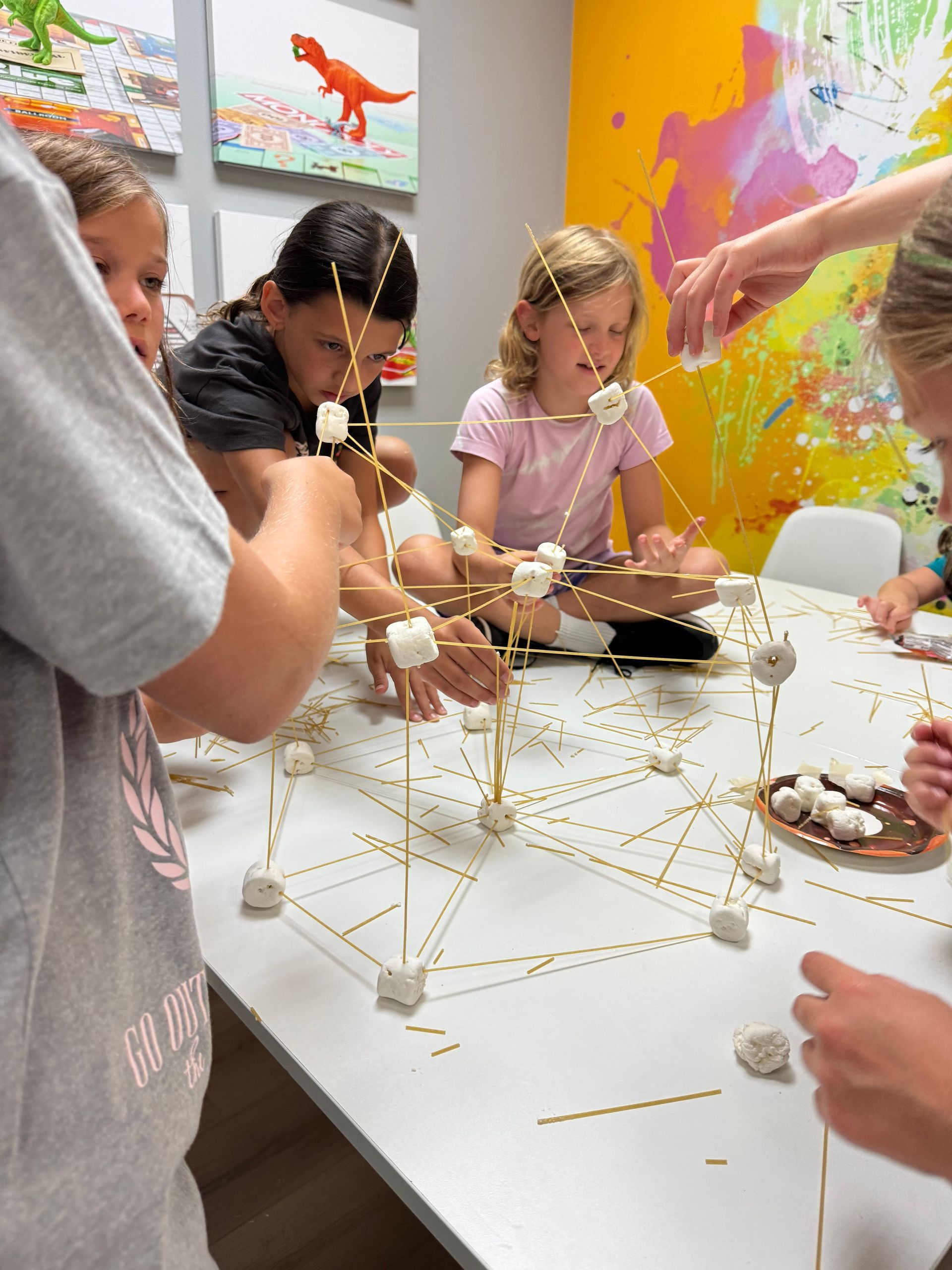 A group of children are sitting around a table making marshmallow pyramids.