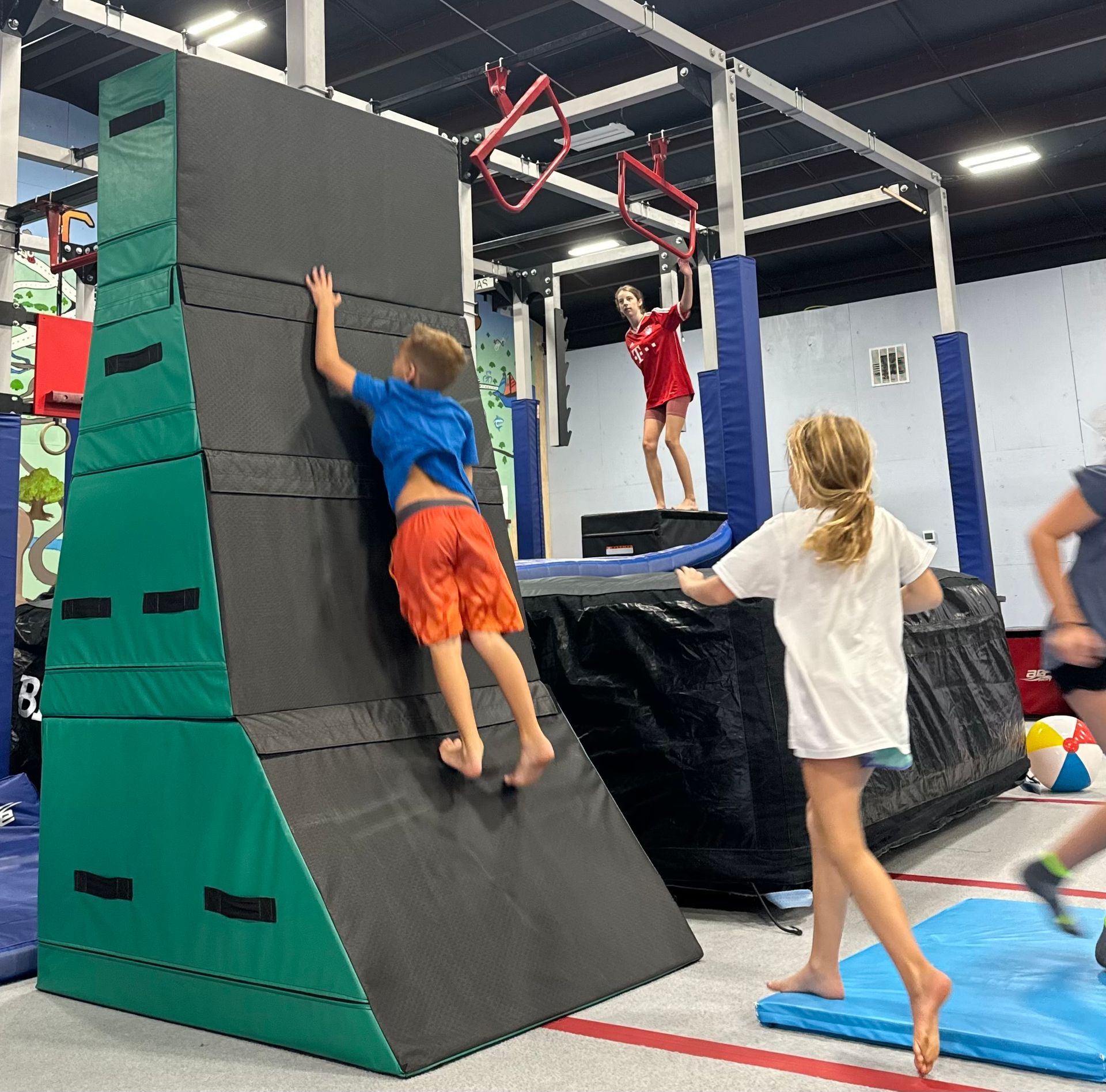 A boy is climbing a wall in a gym while a girl watches.