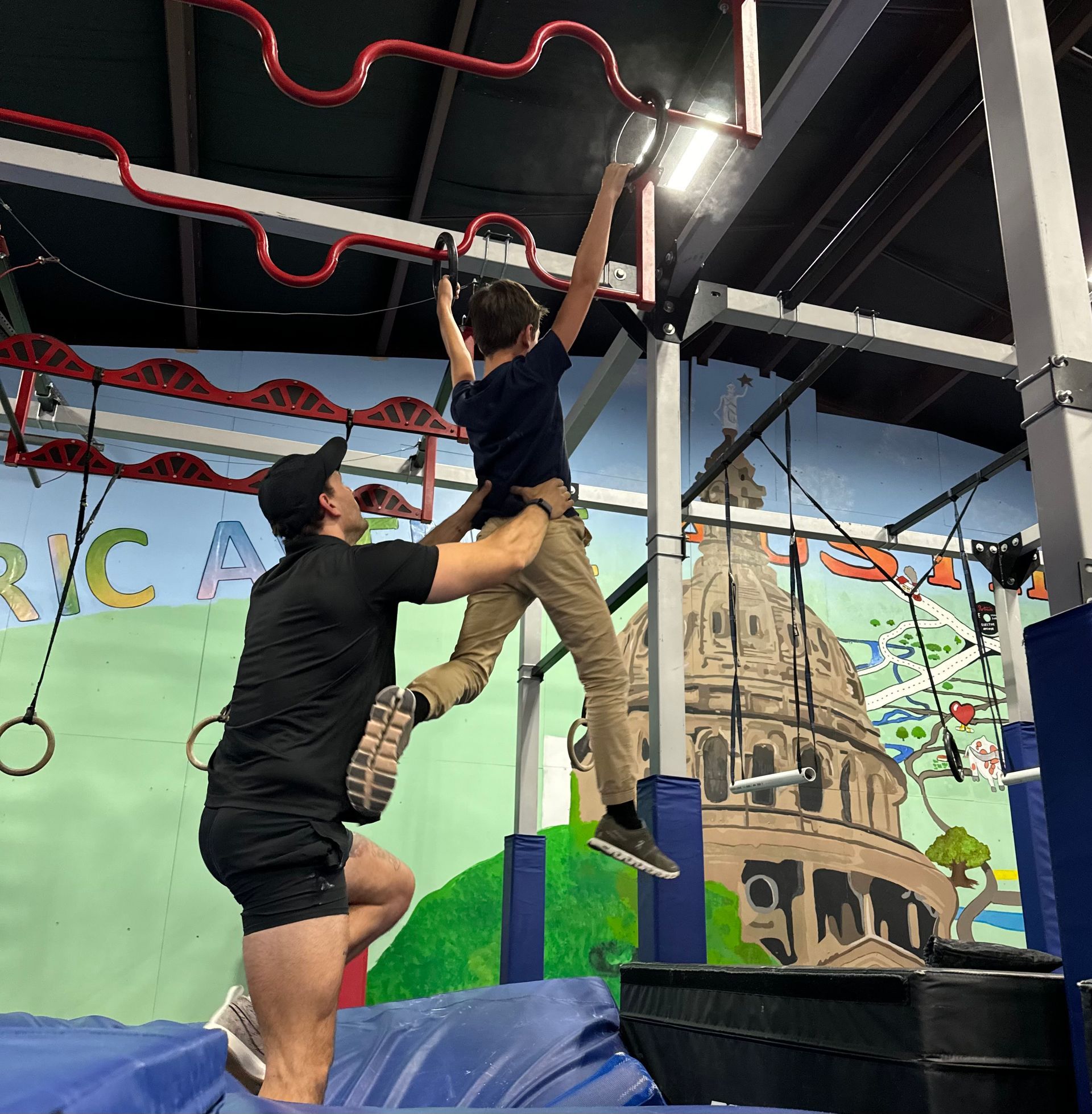 A man is helping a young boy climb a ropes course.