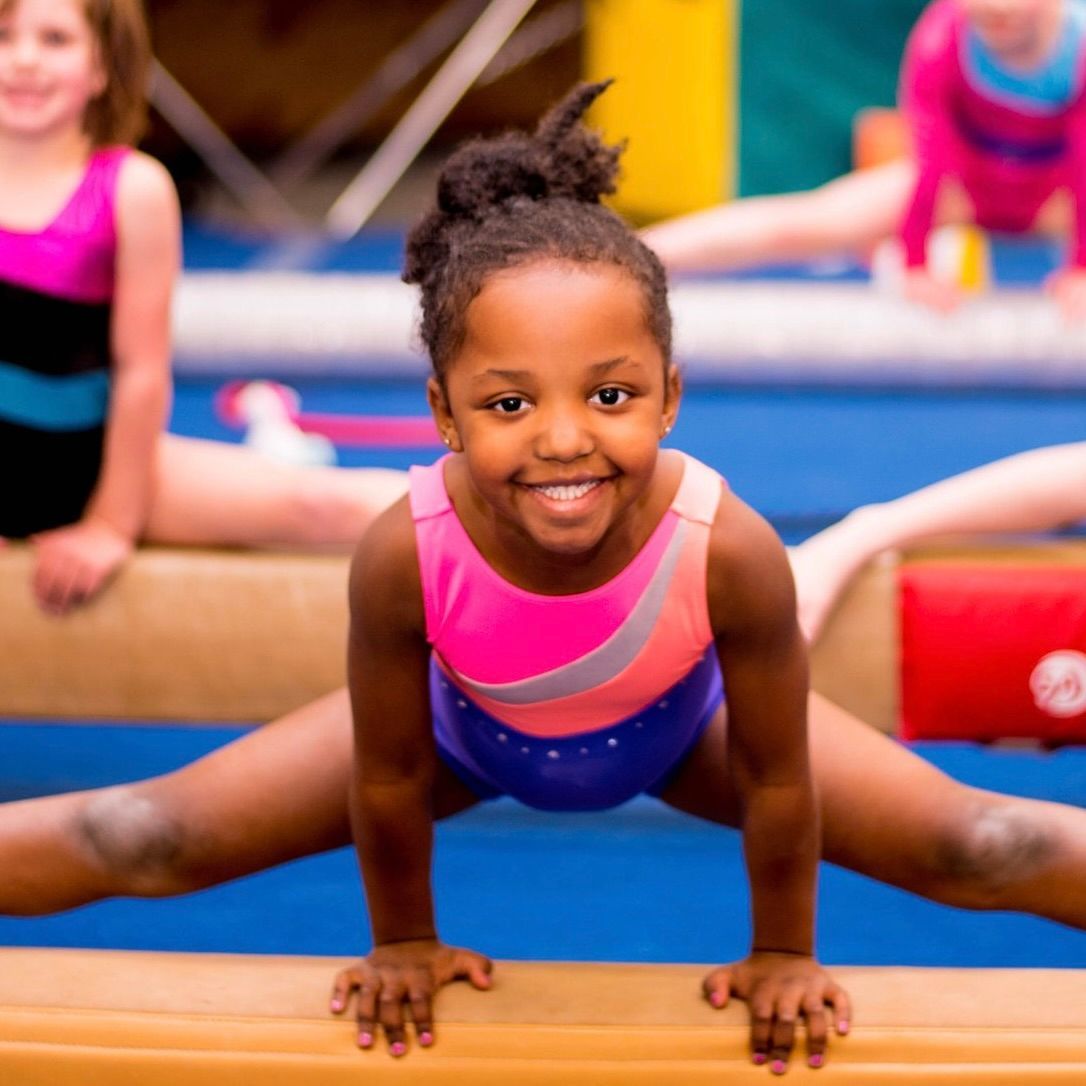 A young girl is doing splits on a balance beam