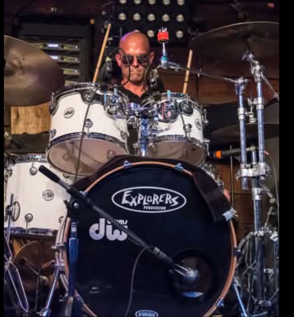 Drummer in sunglasses playing a white drum set at a performance.