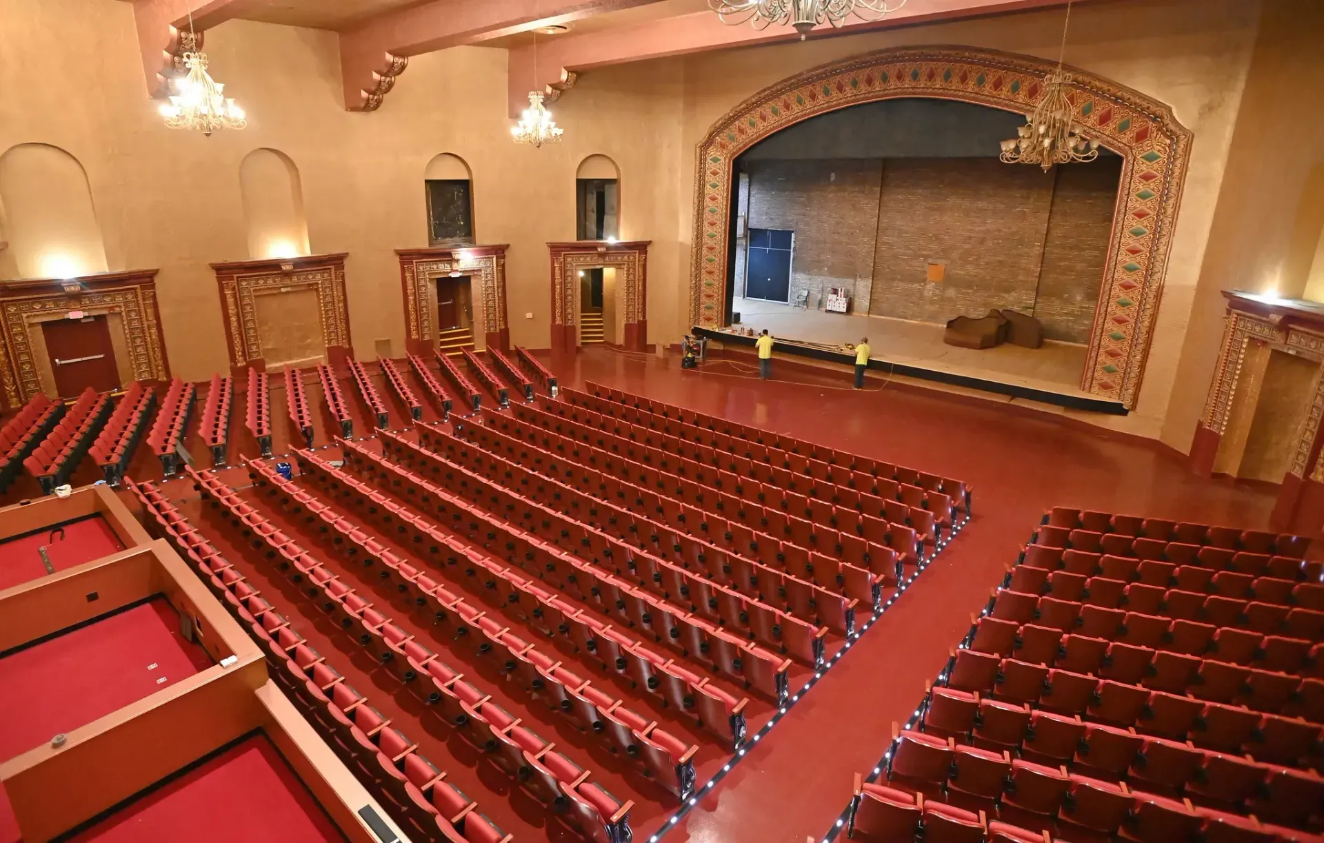 Inside view of a vintage theater, red seating, stage under construction, decorative trim, high angle.