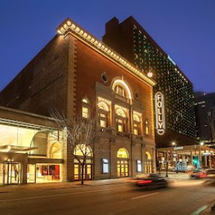 Folly Theater at dusk with illuminated facade, adjacent to a tall hotel on a city street.
