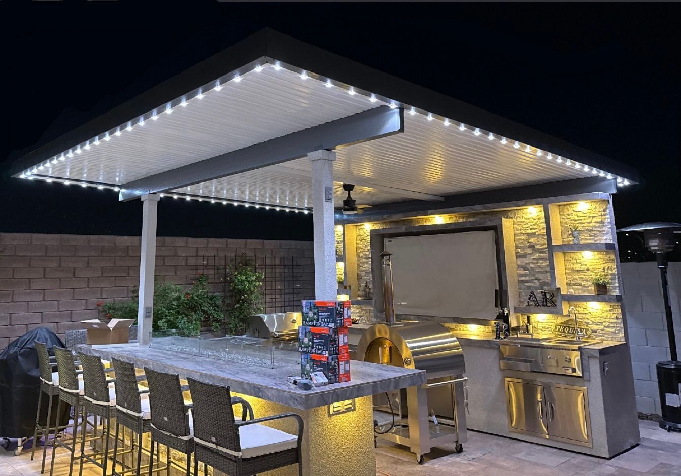 Outdoor kitchen and dining area at night with string lights, bar stools, and a stone counter