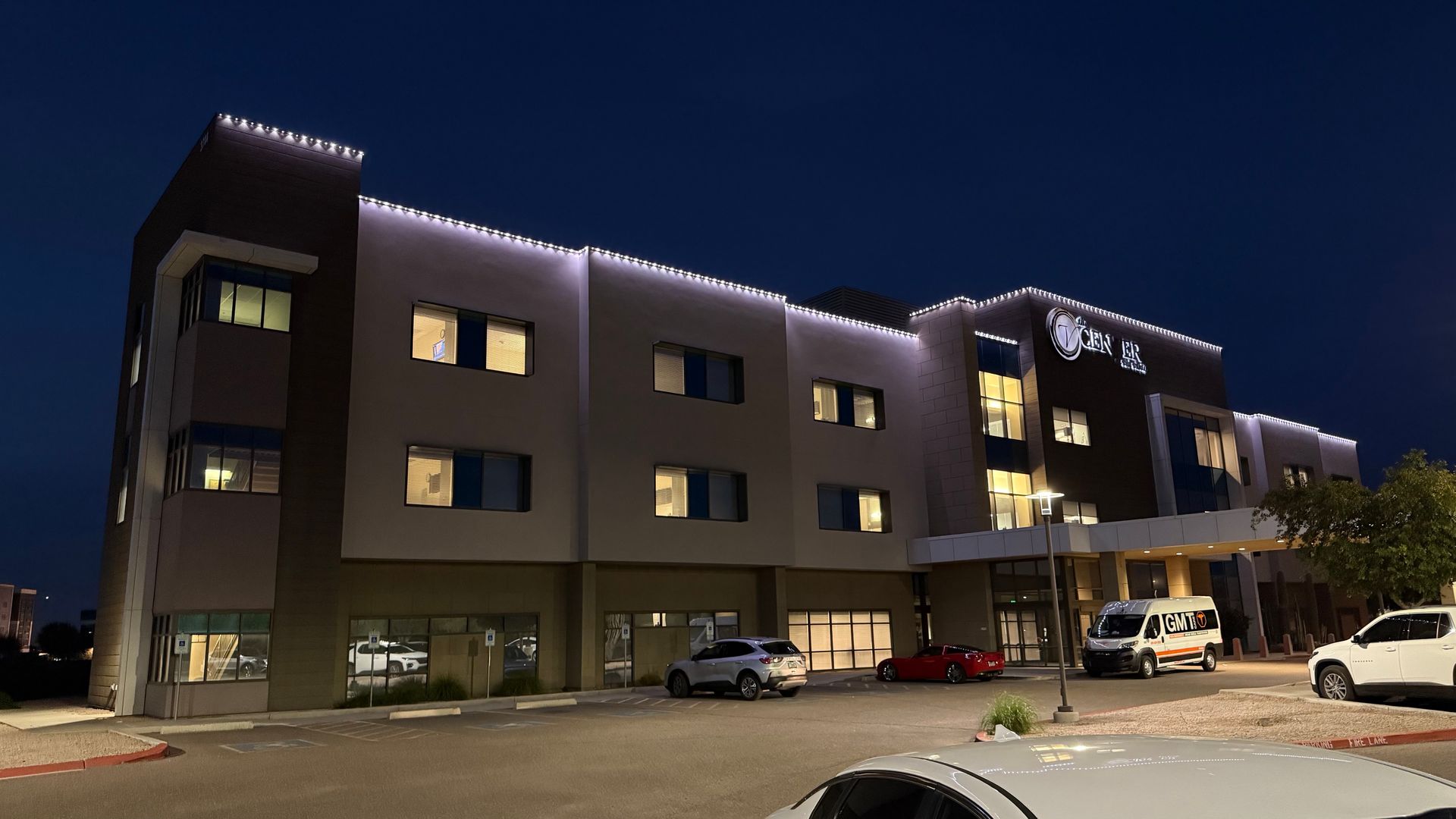 Hotel exterior at night, lit with white lights. Cars parked in front of the building.