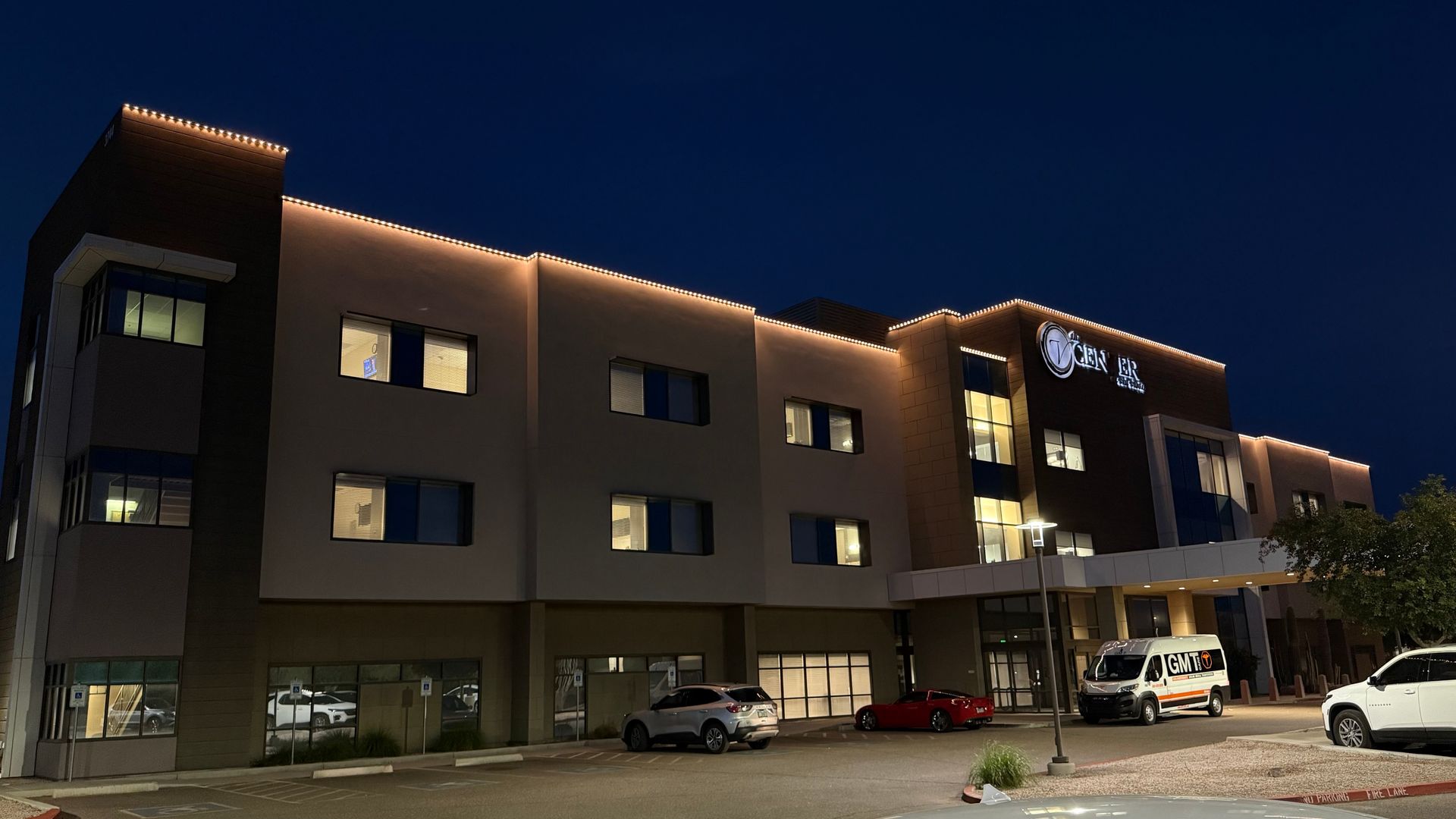 Hotel exterior at night with illuminated roofline. Cars and a van parked in front.