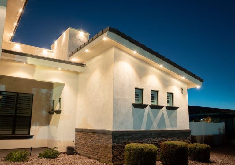 Modern stucco house exterior at dusk with warm lights and stone base trim