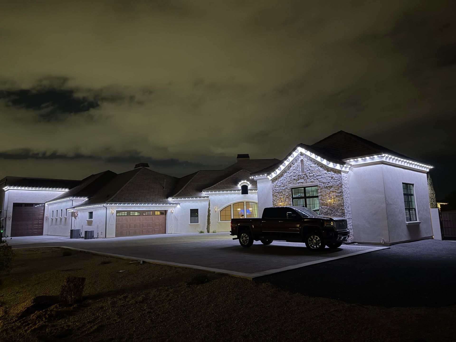 A white house with bright white roofline lights at night, with a dark pickup truck parked in the driveway.