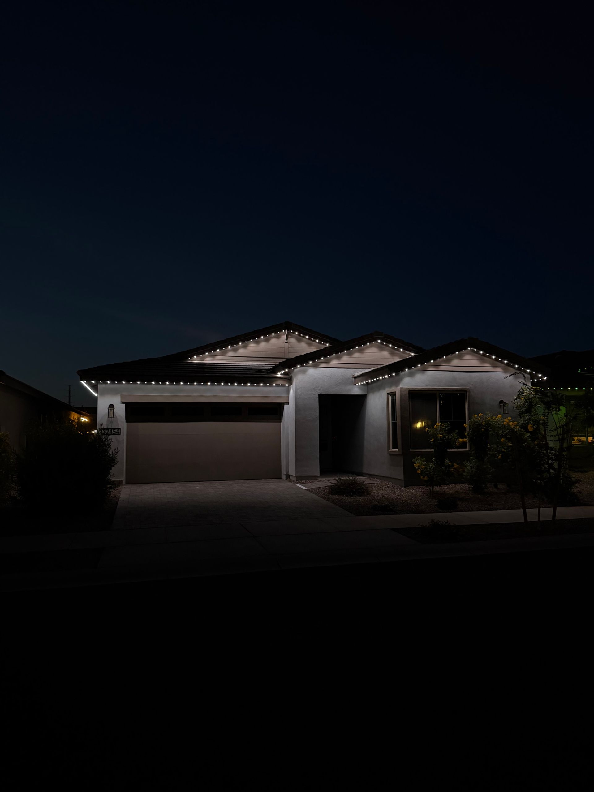 A suburban house at night, illuminated by decorative string lights along the roofline against a dark sky.