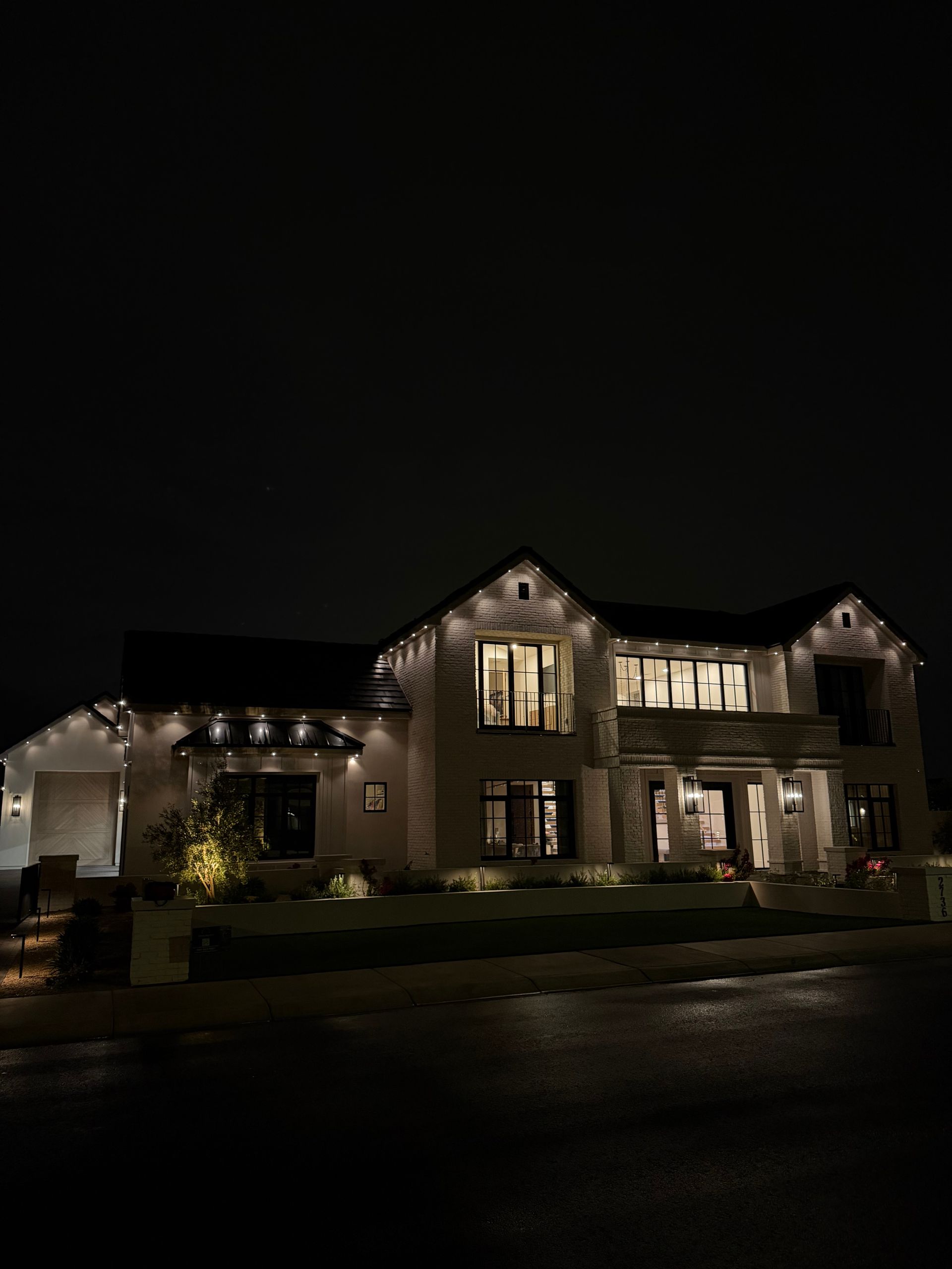 A two-story house at night with glowing architectural roofline lights and warm interior lighting shining through windows.