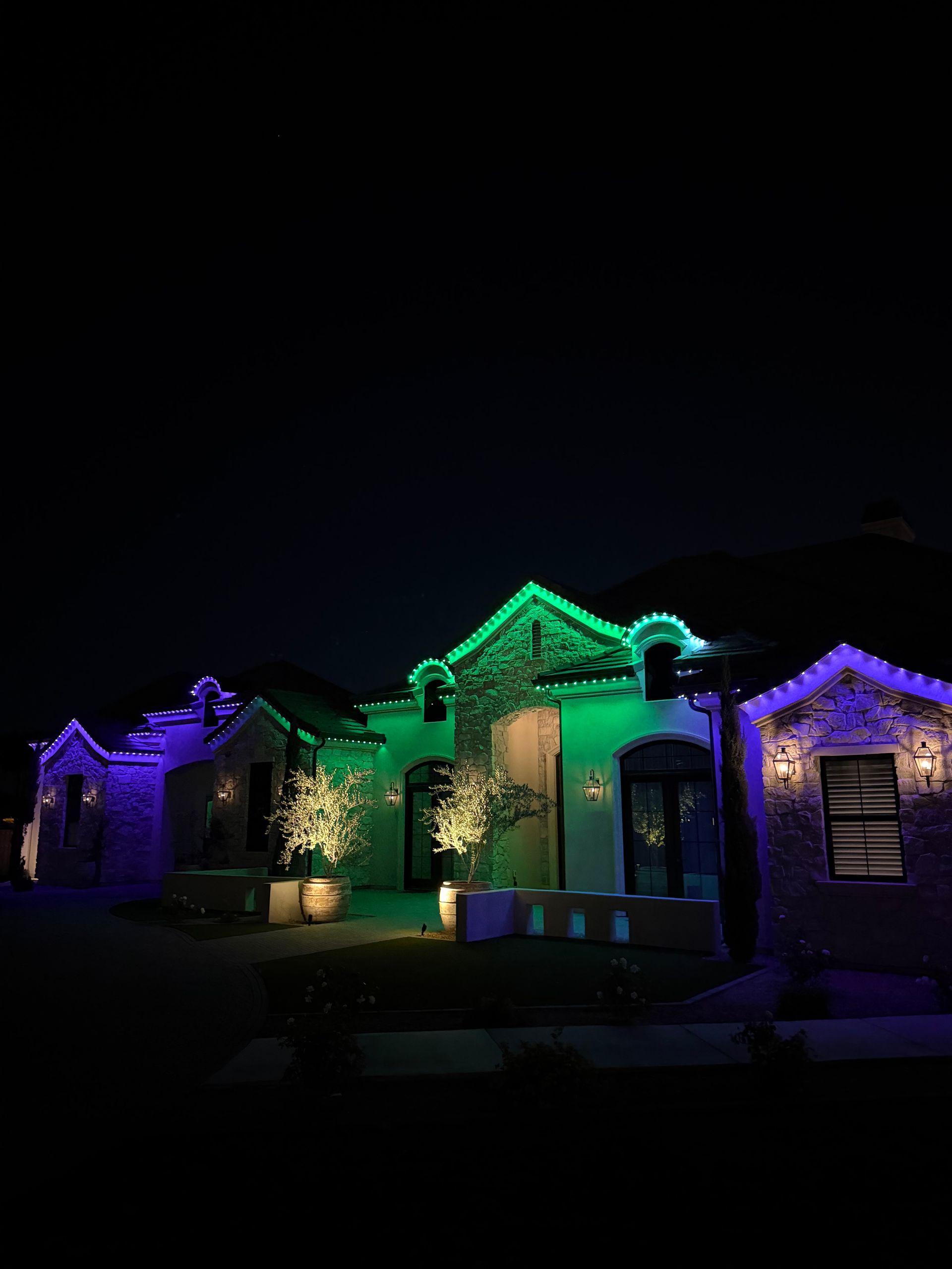 House at night lit with green, purple, and blue decorative lights on the roof and porch