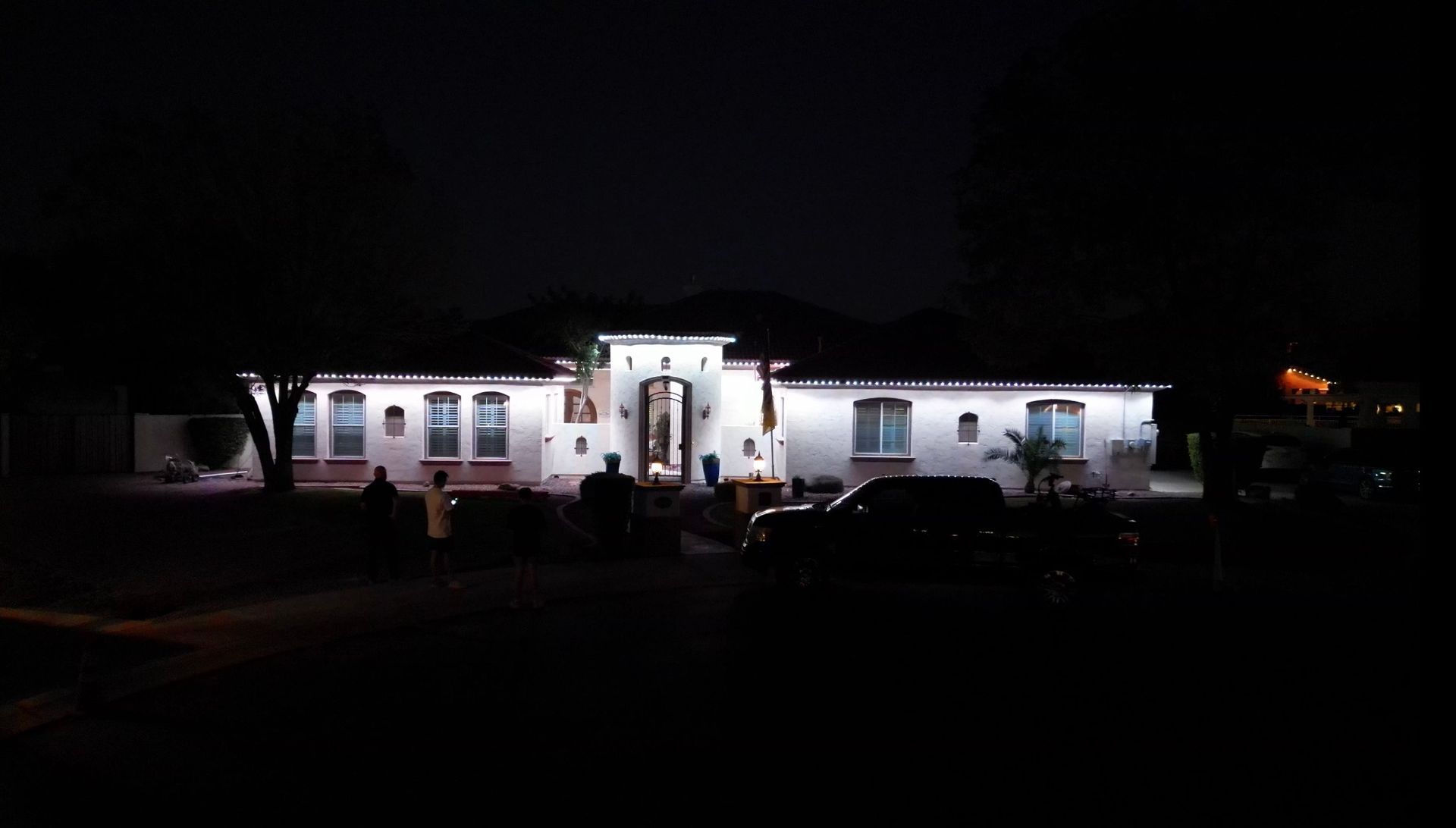 Nighttime view of a lit white house with a central entrance and dark foreground