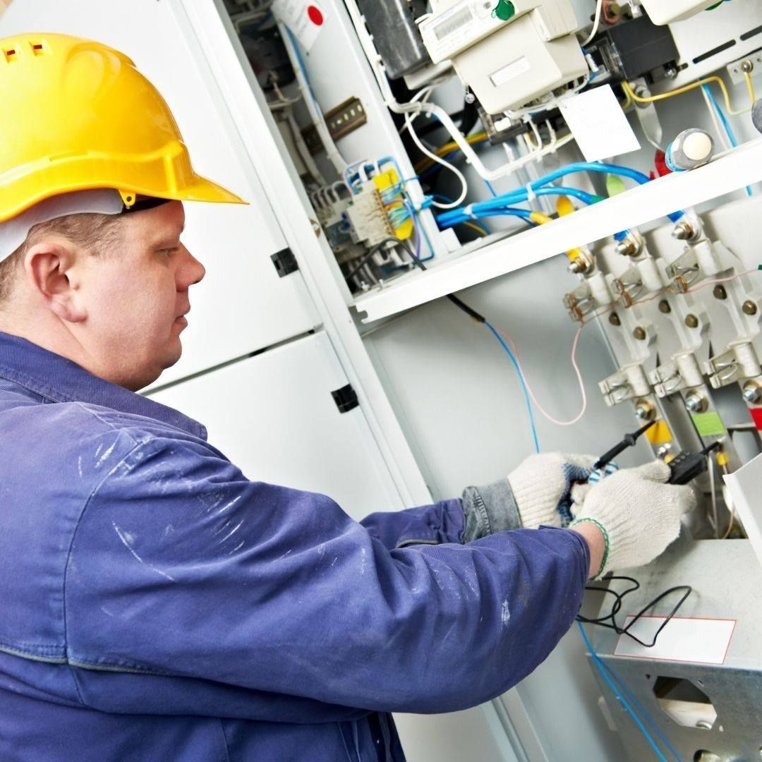 A man wearing a yellow hard hat is working on an electrical box