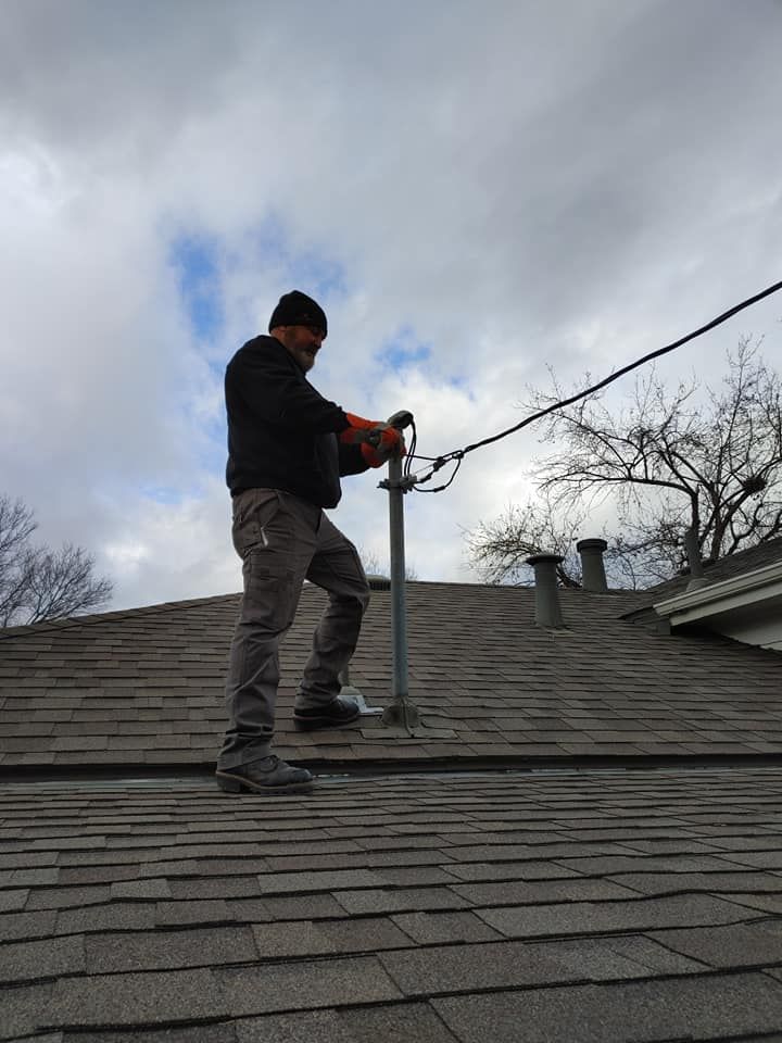A man is standing on top of a roof holding a tool.