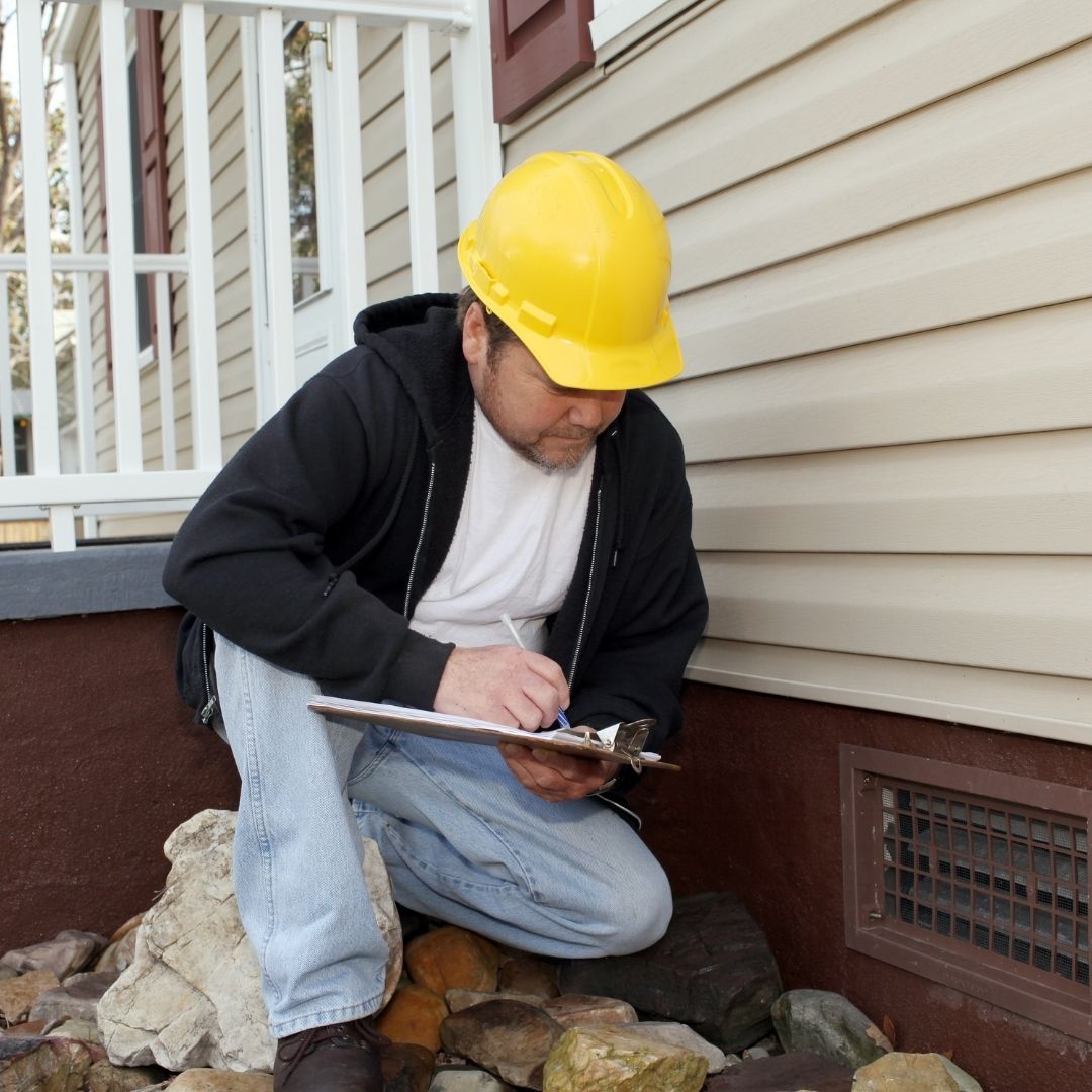 A man wearing a yellow hard hat is writing on a clipboard