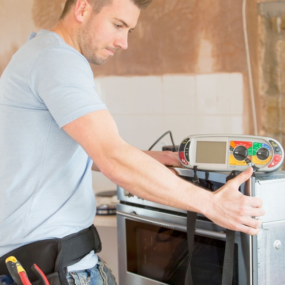 A man wearing a tool belt is working on an oven