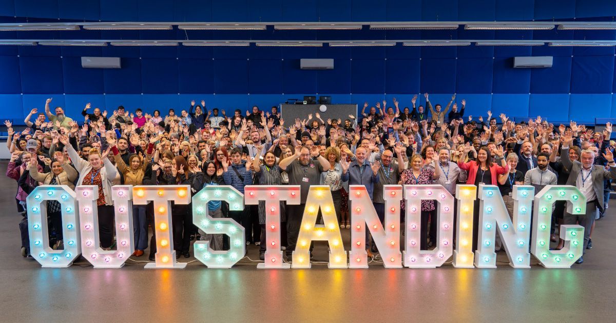 A large group of people are standing in front of a sign that says outstanding.