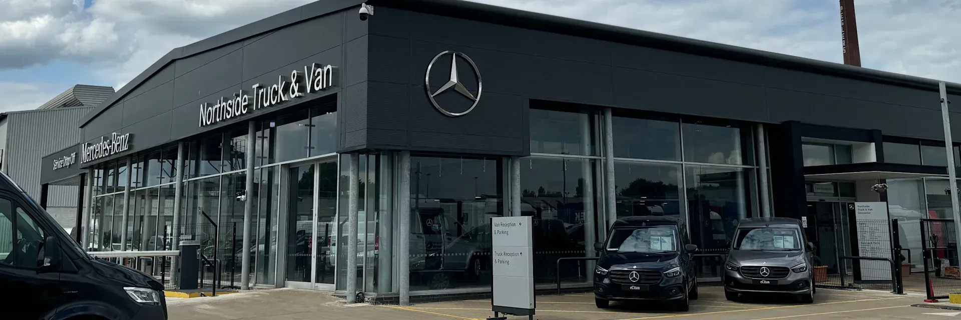 A mercedes benz dealership with cars parked in front of it.