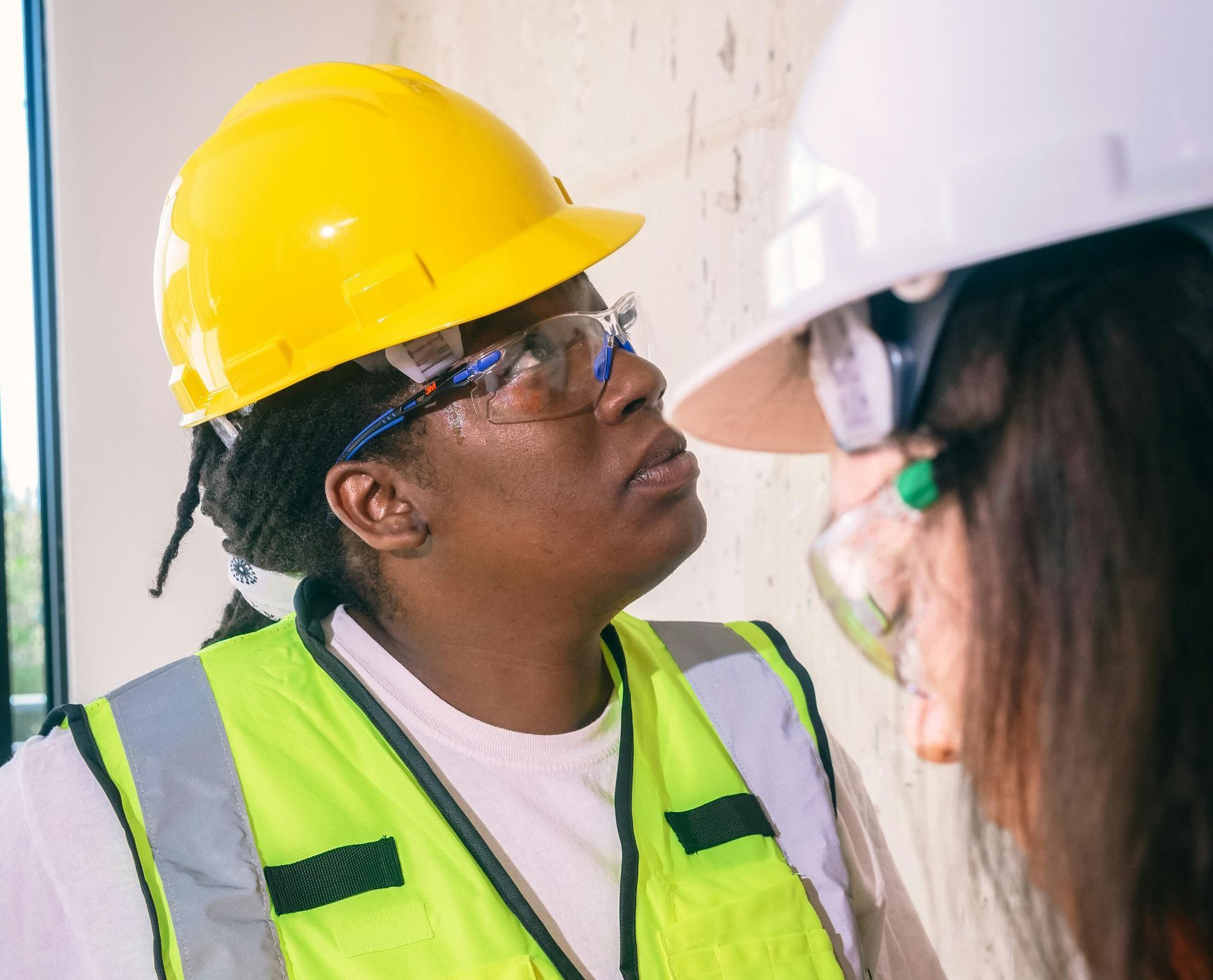 A woman wearing a hard hat and safety vest is talking to another woman.
