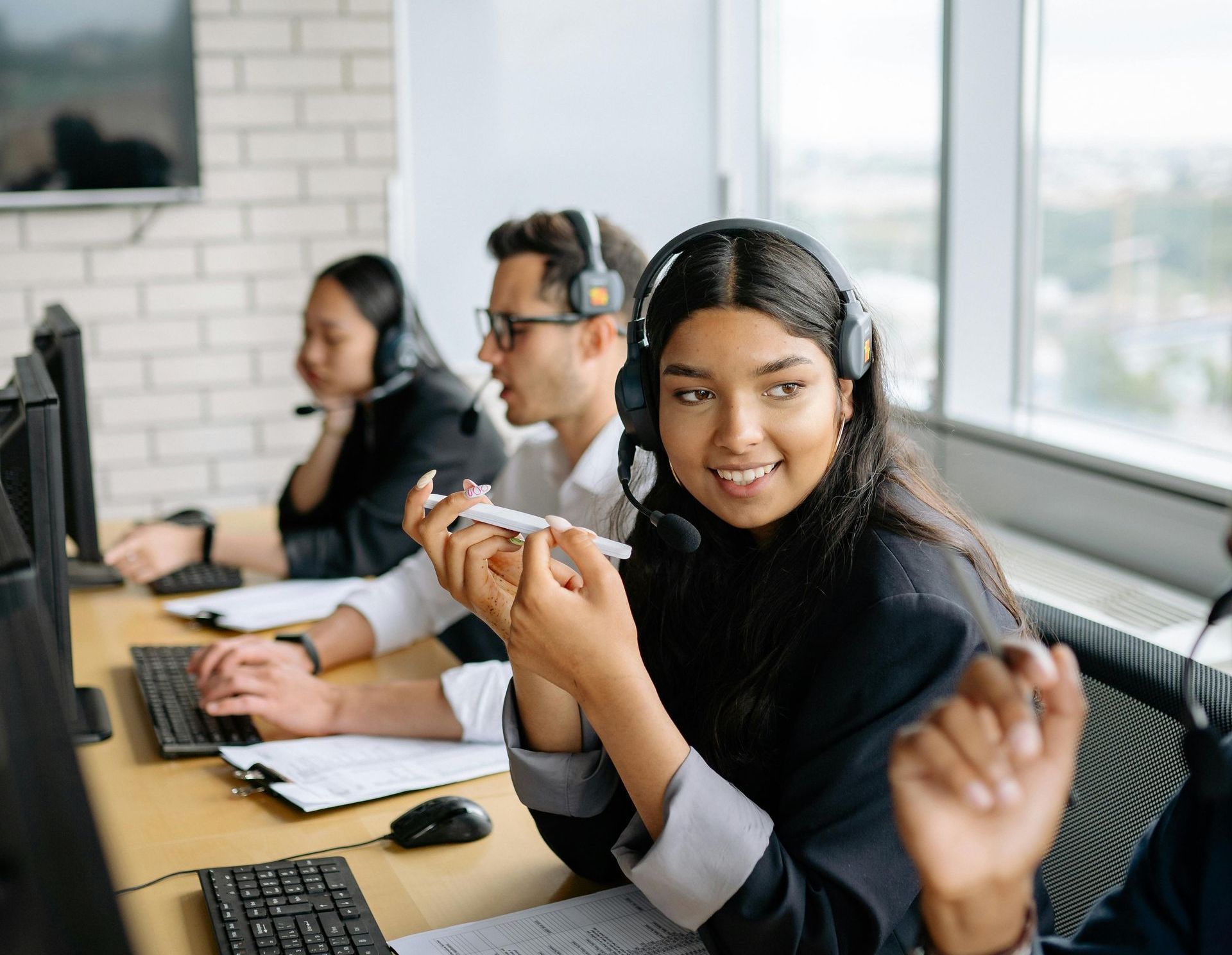 A woman is wearing a headset while sitting at a desk in front of a computer.