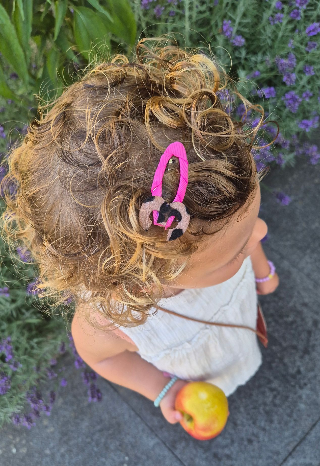 Meisje met krullend haar, met een roze haarclip met luipaardprint, houdt een appel vast.