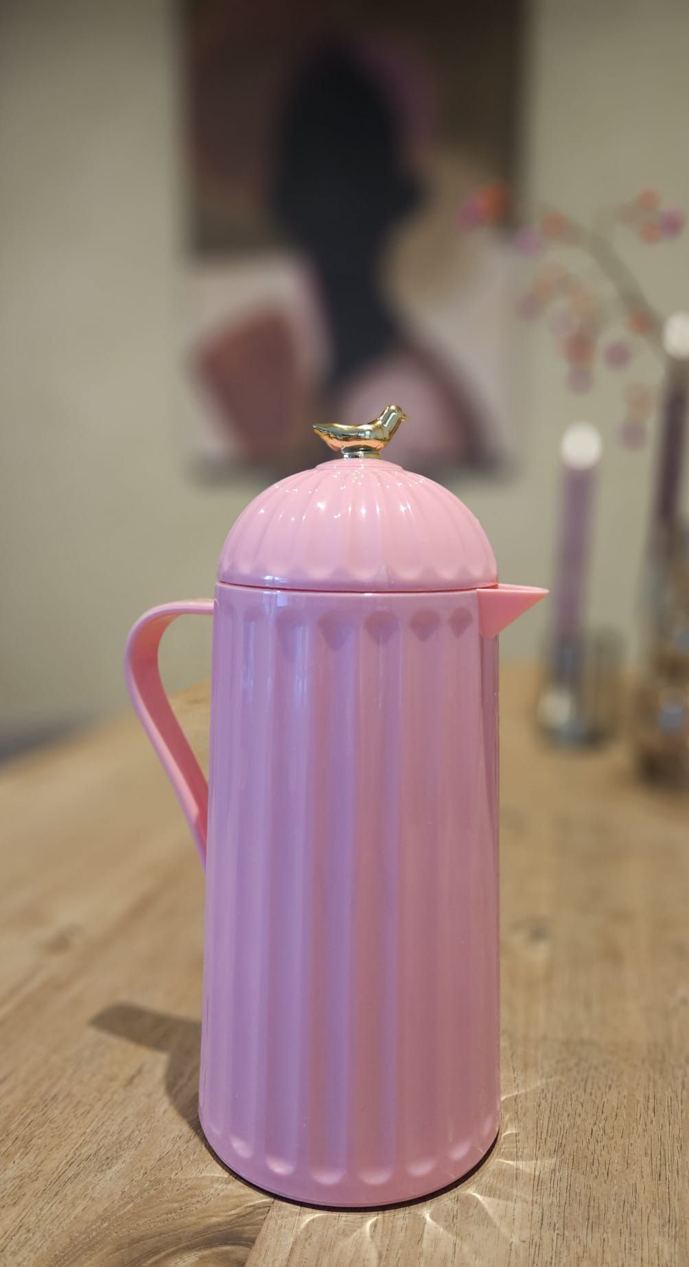 Roze, geïsoleerde karaf op een houten tafel, met een goudkleurig vogeltje op het deksel.
