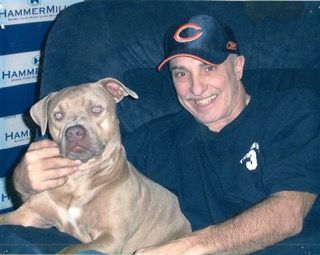 A man wearing a hat with the letter c on it holds a dog