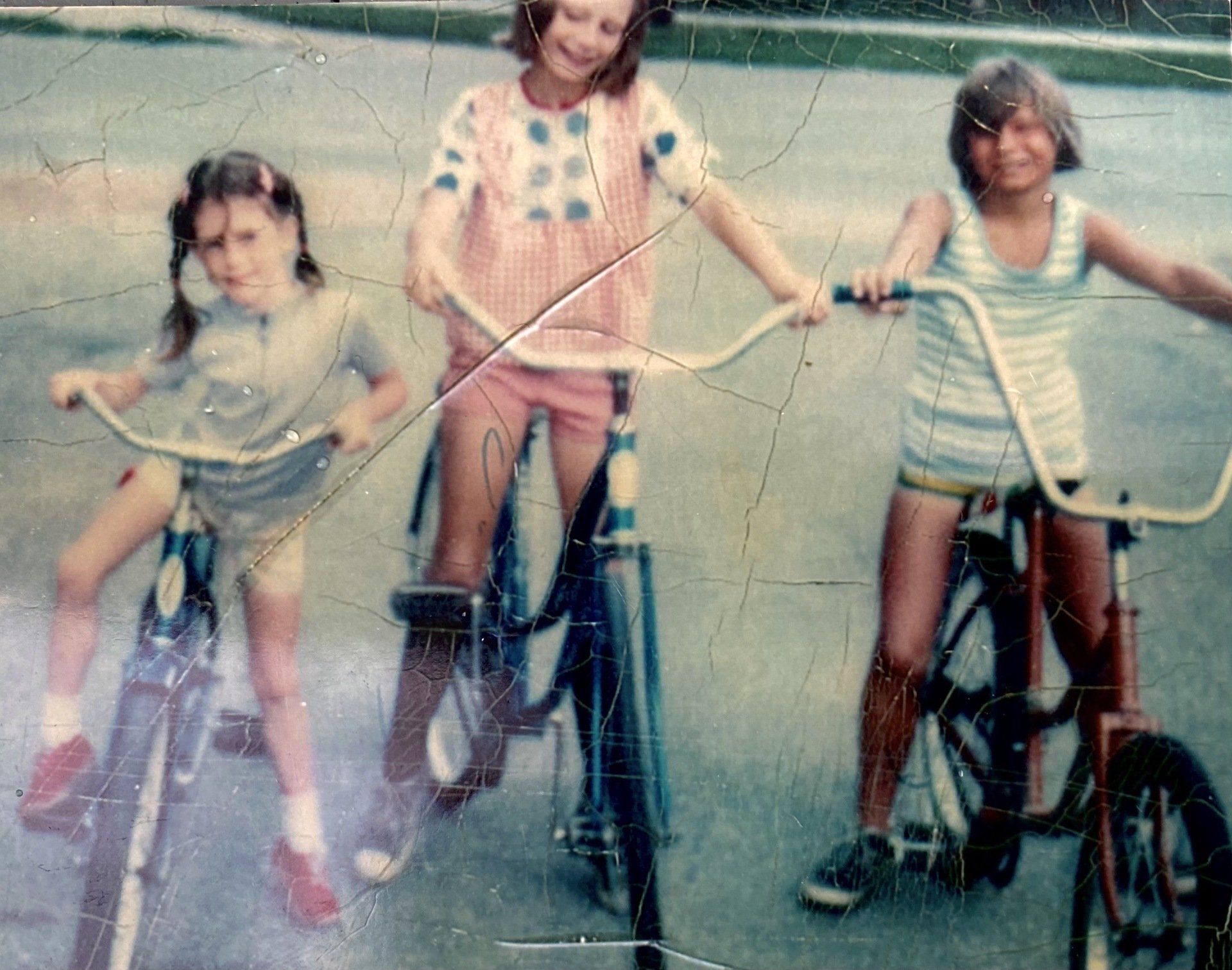 Three young girls are riding bicycles on a street