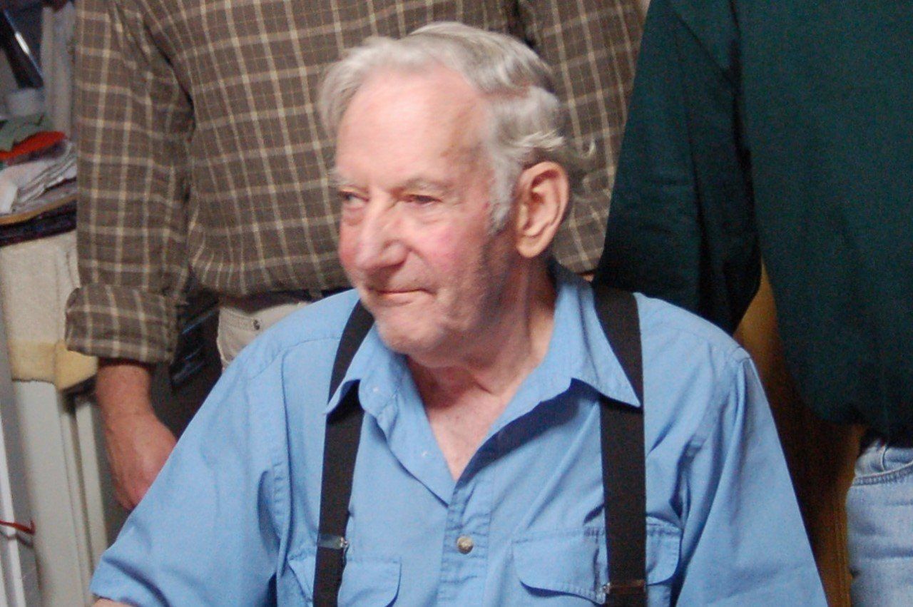 An elderly man wearing suspenders and a blue shirt