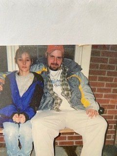 A man and a boy are sitting on a bench in front of a brick building.