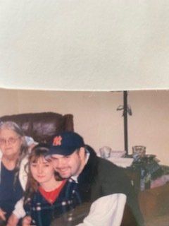 A man in a ny hat is sitting next to a little girl in a living room.